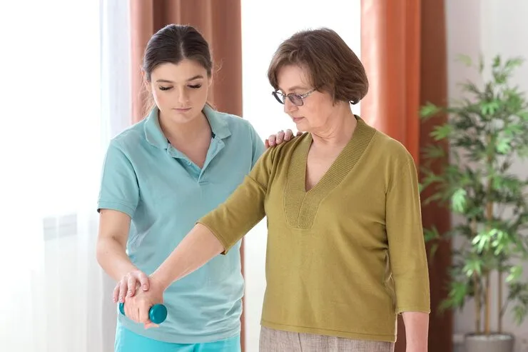 10 qualities of a good caregiver — young caregiver in scrubs assisting an elderly woman with mobility at home